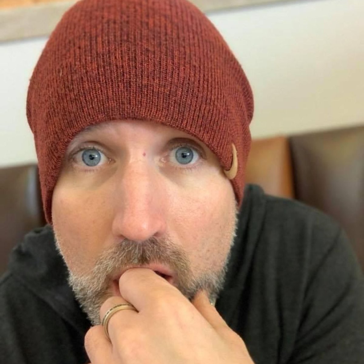 Neil Martin in a red beanie hat, looking into the camera with his hand to his chin
