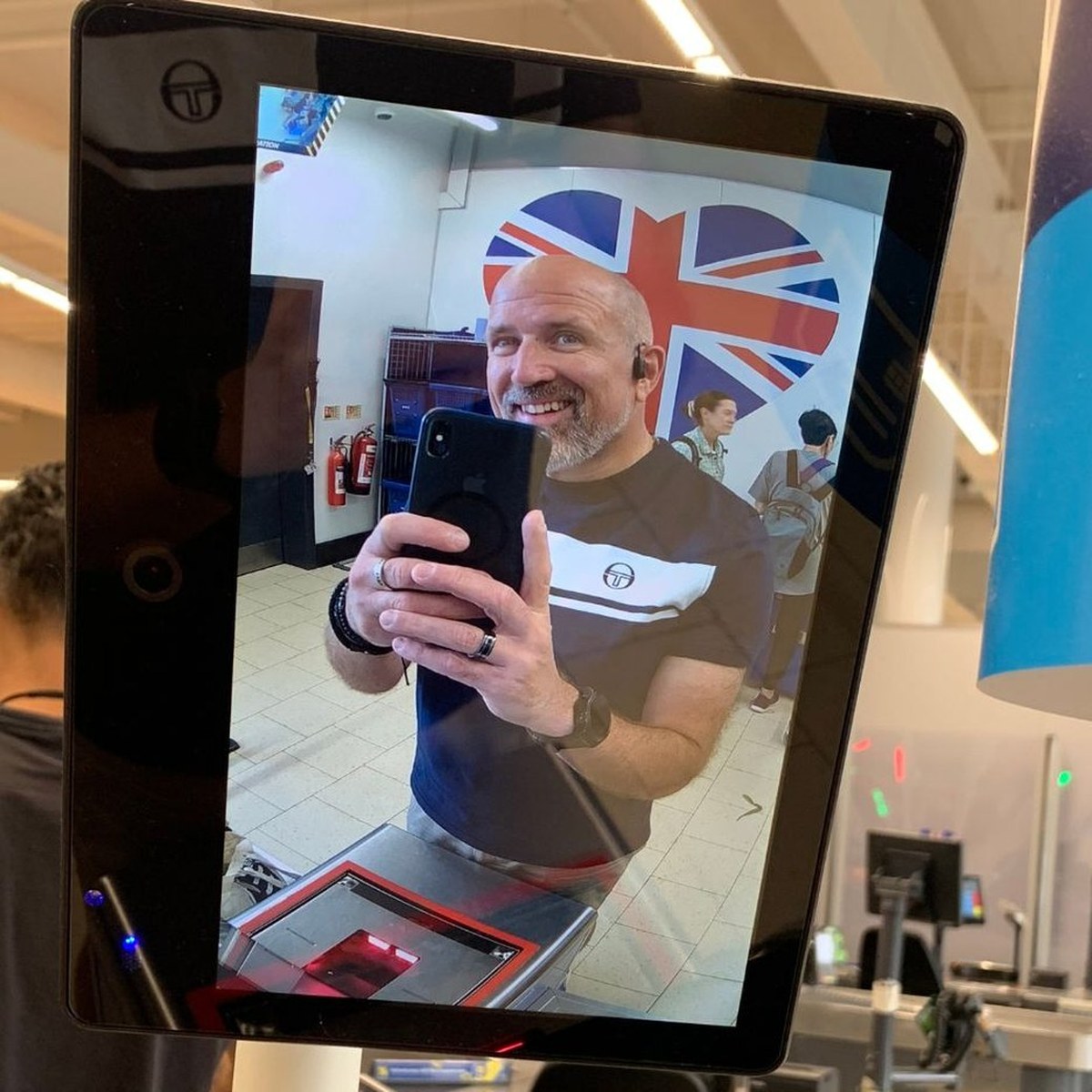 Neil grinning as he snaps a photo of himself on a supermarket self-checkout camera screen