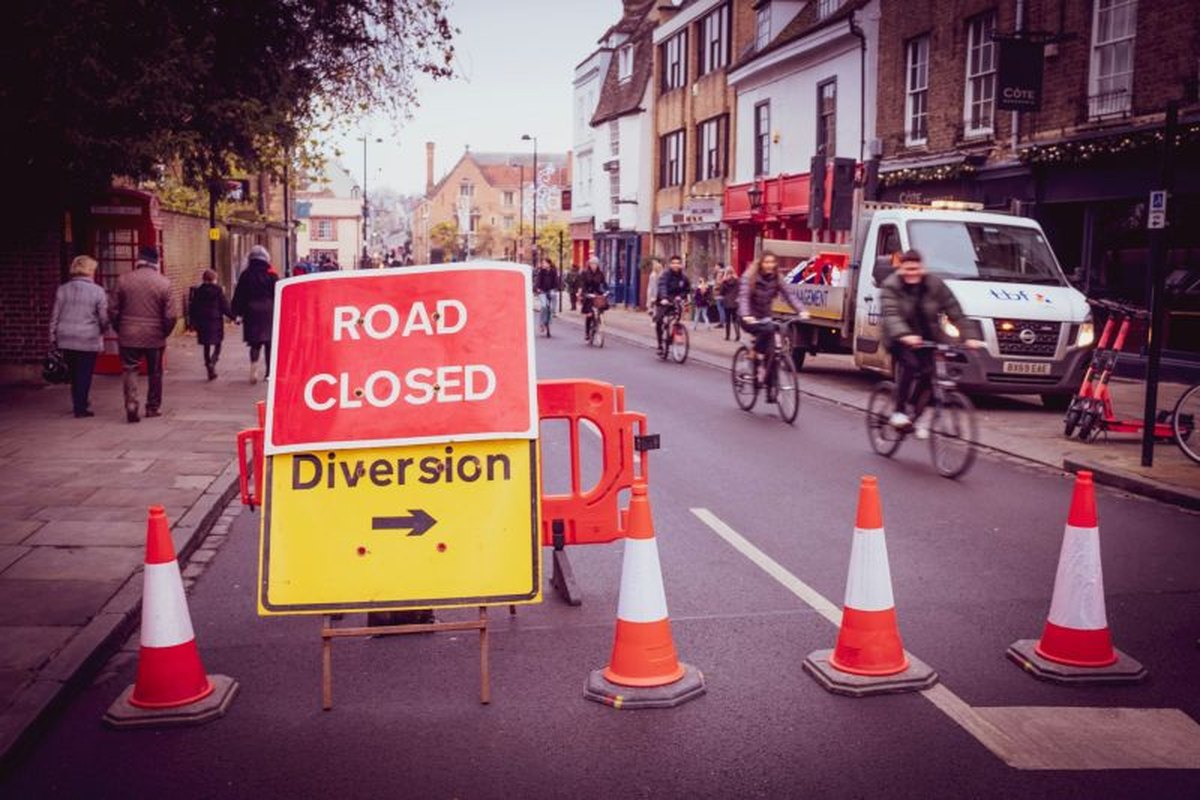 A road closed and diversion sign surrounded by traffic cones on a busy street in Cheltenham