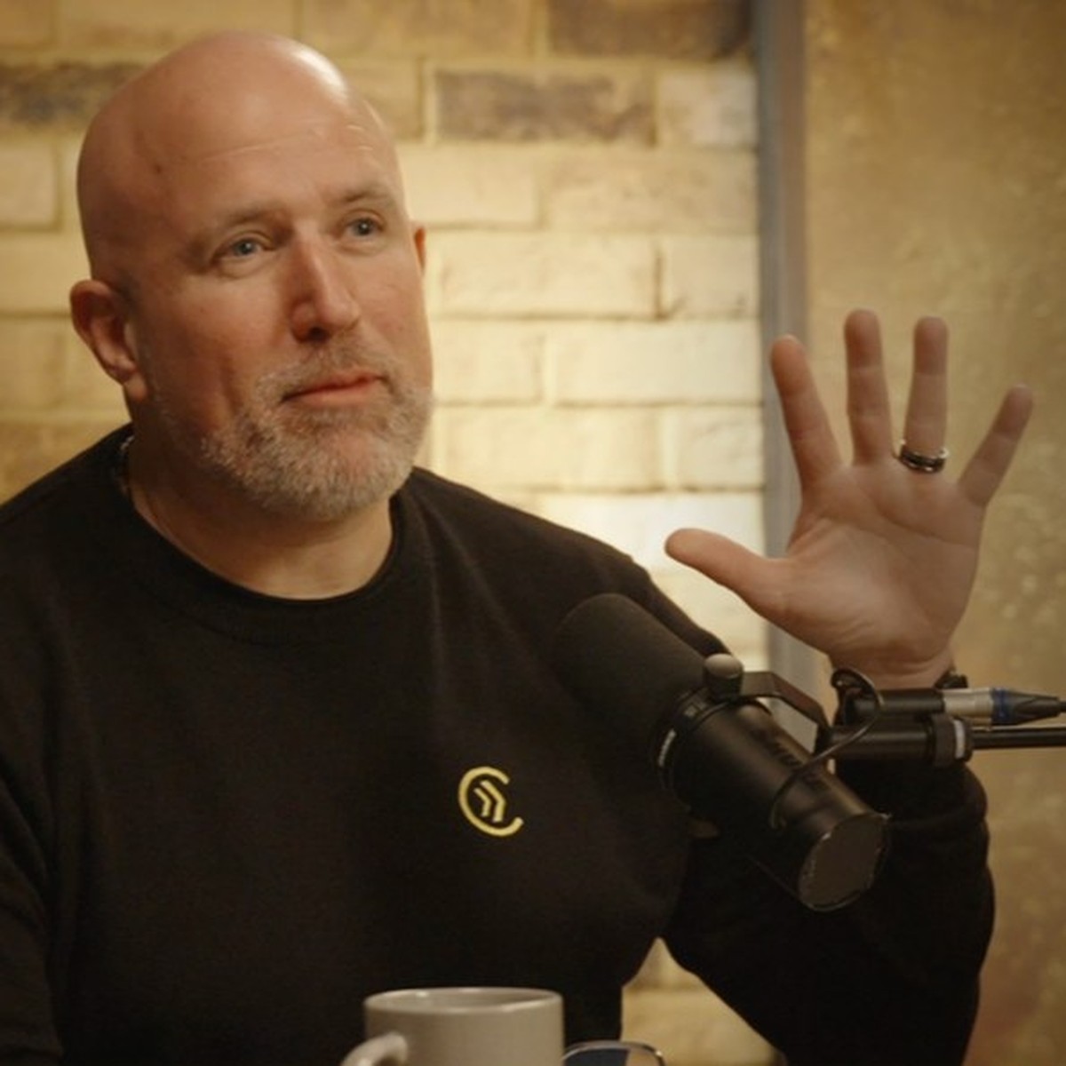 Neil Martin speaking into a podcast microphone with one hand raised