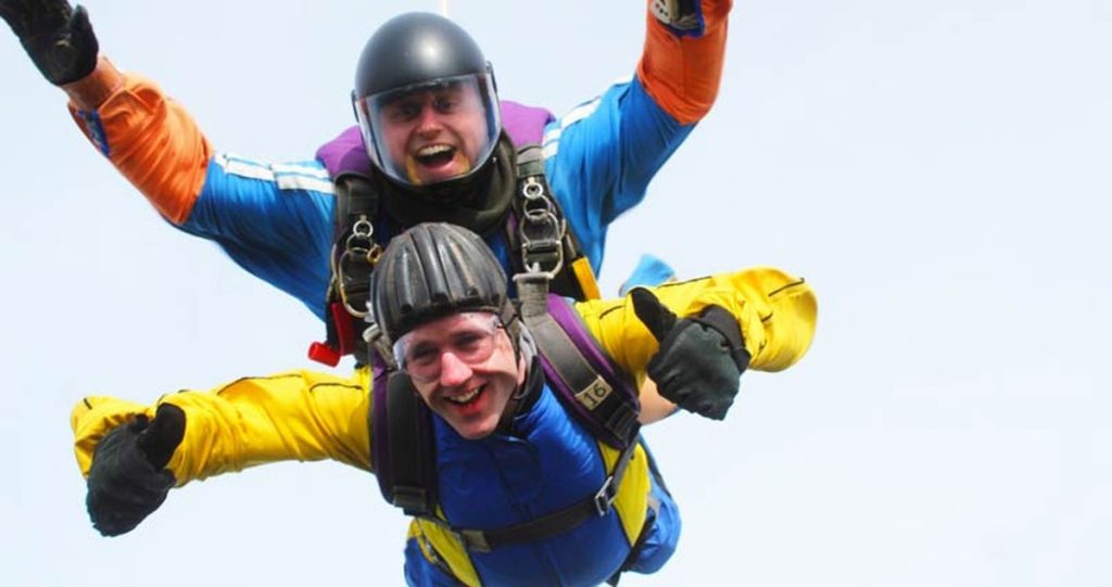 Neil Martin in freefall, arms out, strapped to his tandem instructor
