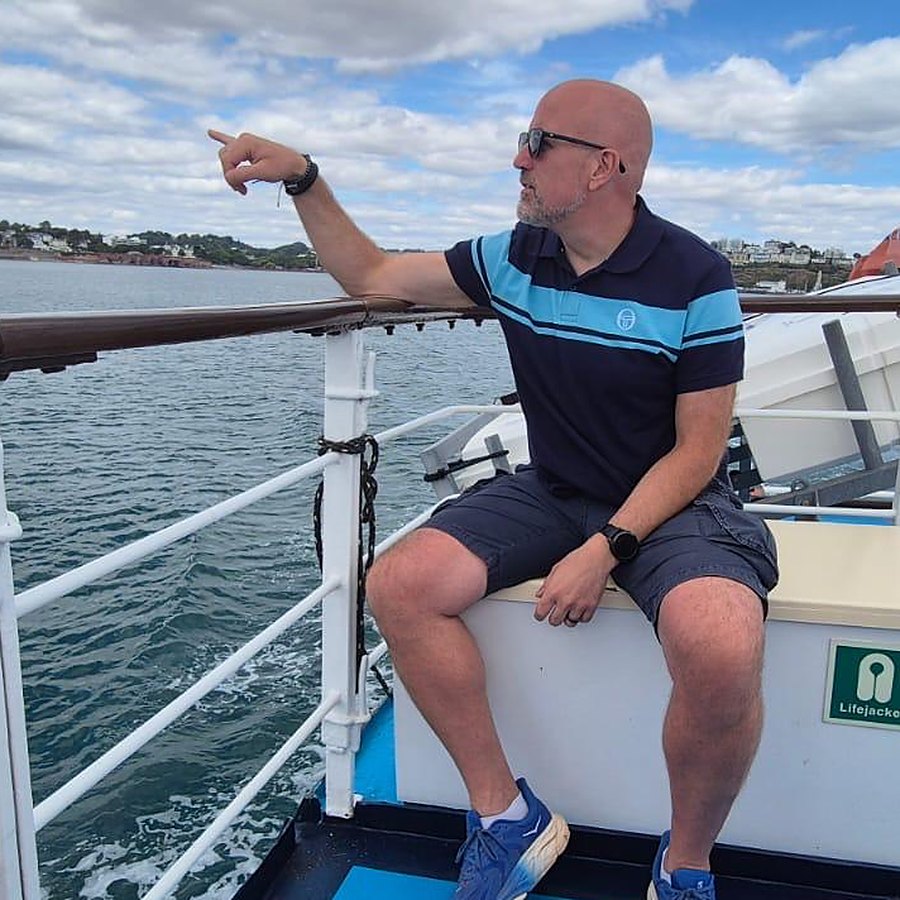 Neil Martin on a boat, pointing out to sea