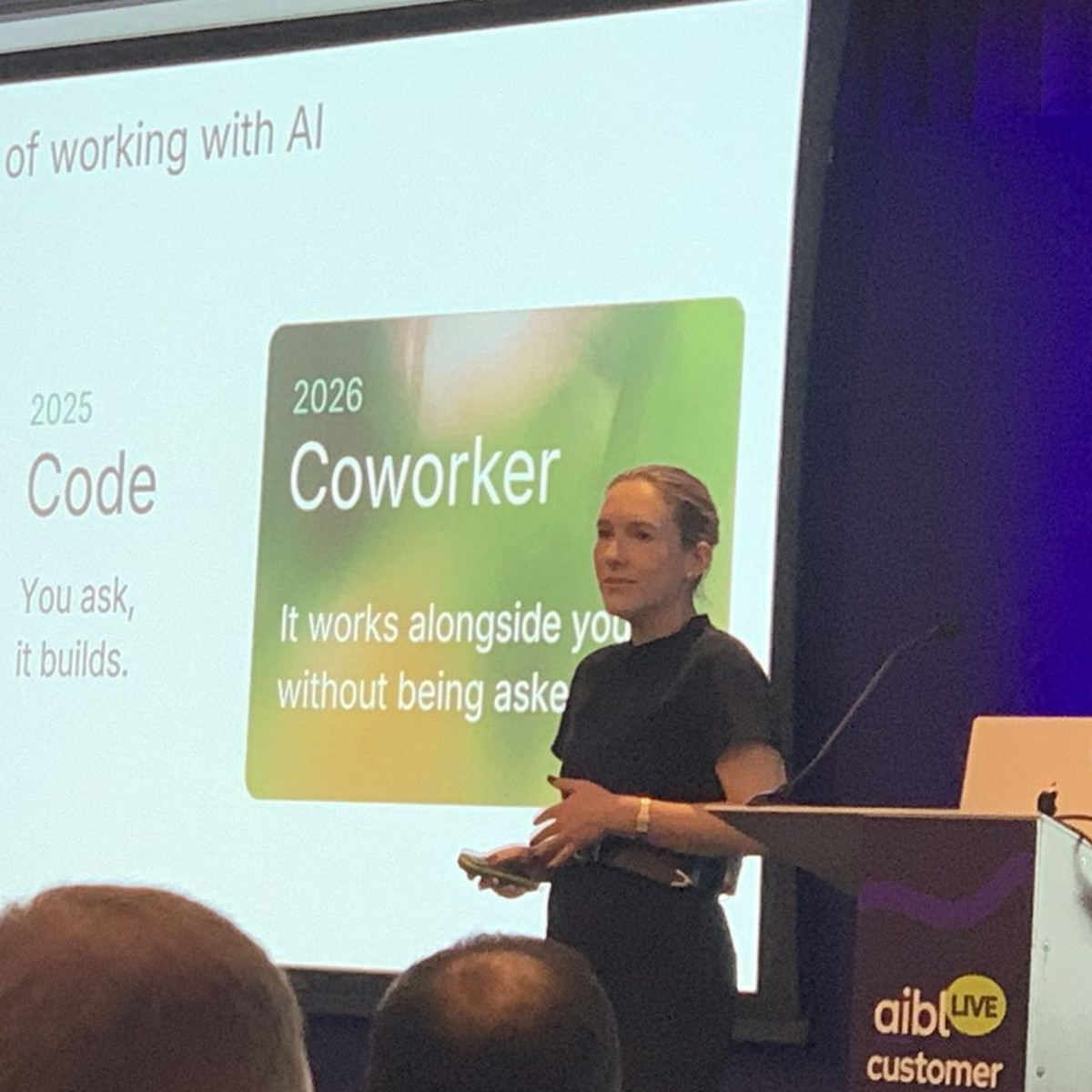 Rebecca Okin of Sierra speaking at a lectern on stage at aiblLIVE London, next to a slide about AI as a coworker